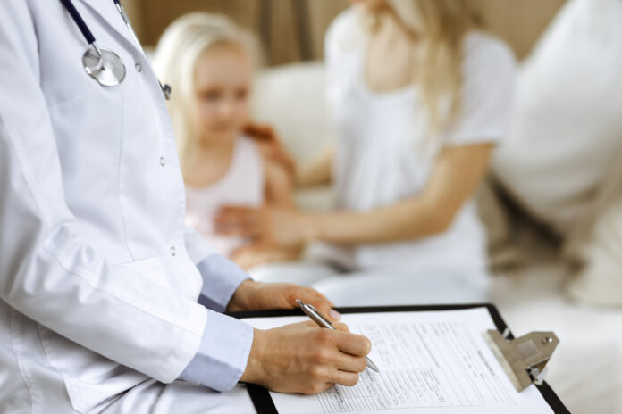 Doctor and patient. Pediatrician using clipboard while examining little girl with her mother at home. Happy cute caucasian child at medical exam. Medicine concept